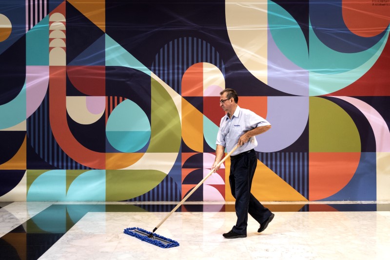 Person mopping a glossy floor in front of a colorful geometric mural on the wall.