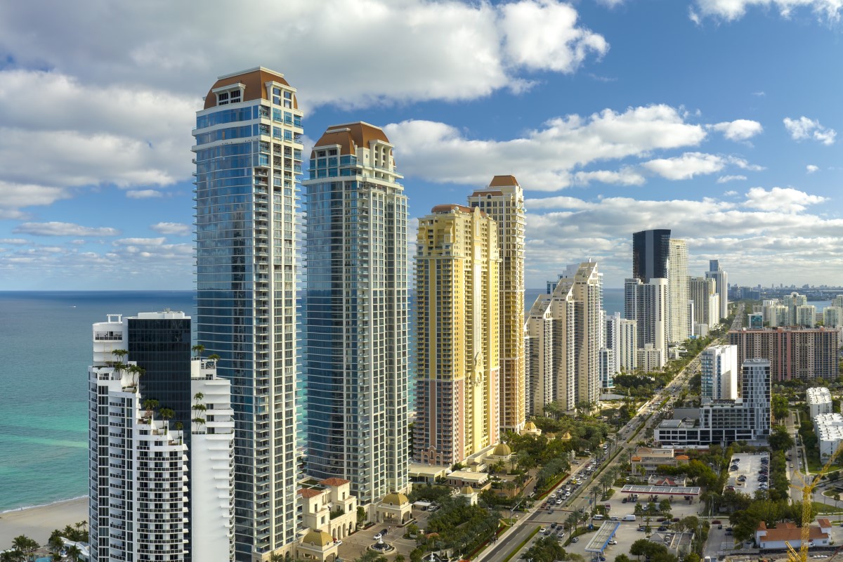 Aerial view of a coastal cityscape with tall skyscrapers and nearby beach.