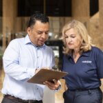 Two people reviewing a document on a clipboard in an office lobby.