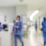 Blurred view of medical staff in a hospital corridor with bright lighting.