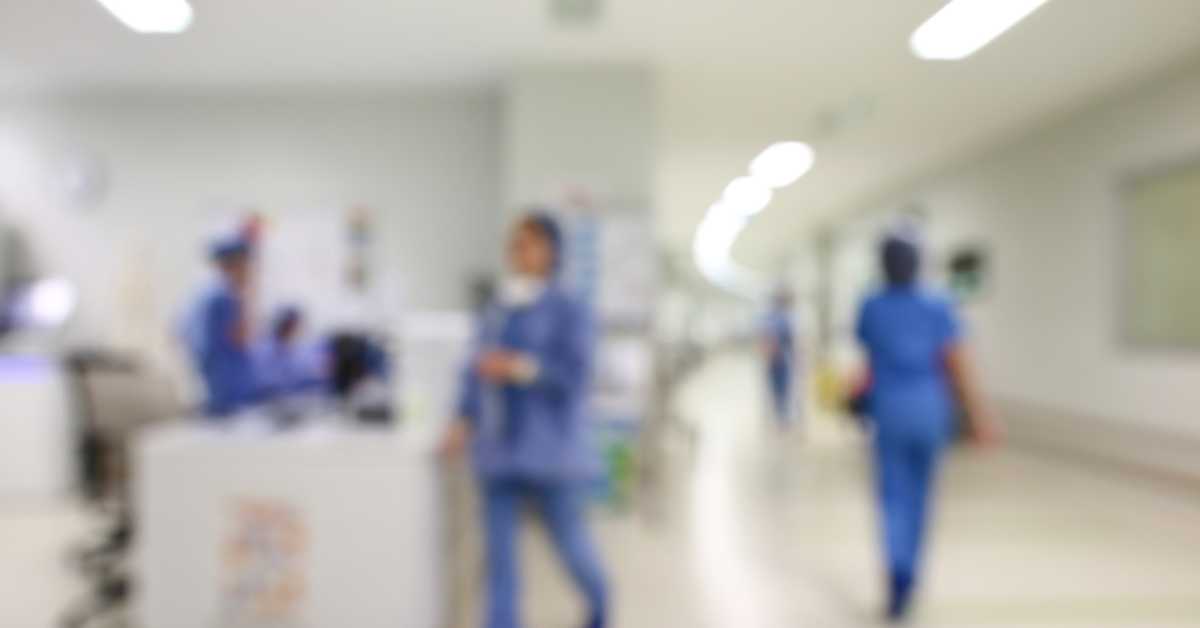 Blurred view of medical staff in a hospital corridor with bright lighting.