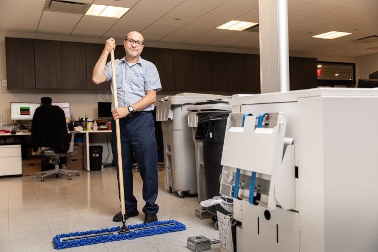 Person mopping the floor in an office setting with desks and equipment.