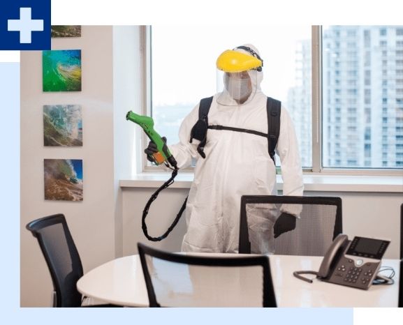 Person in protective gear disinfecting an office conference room.