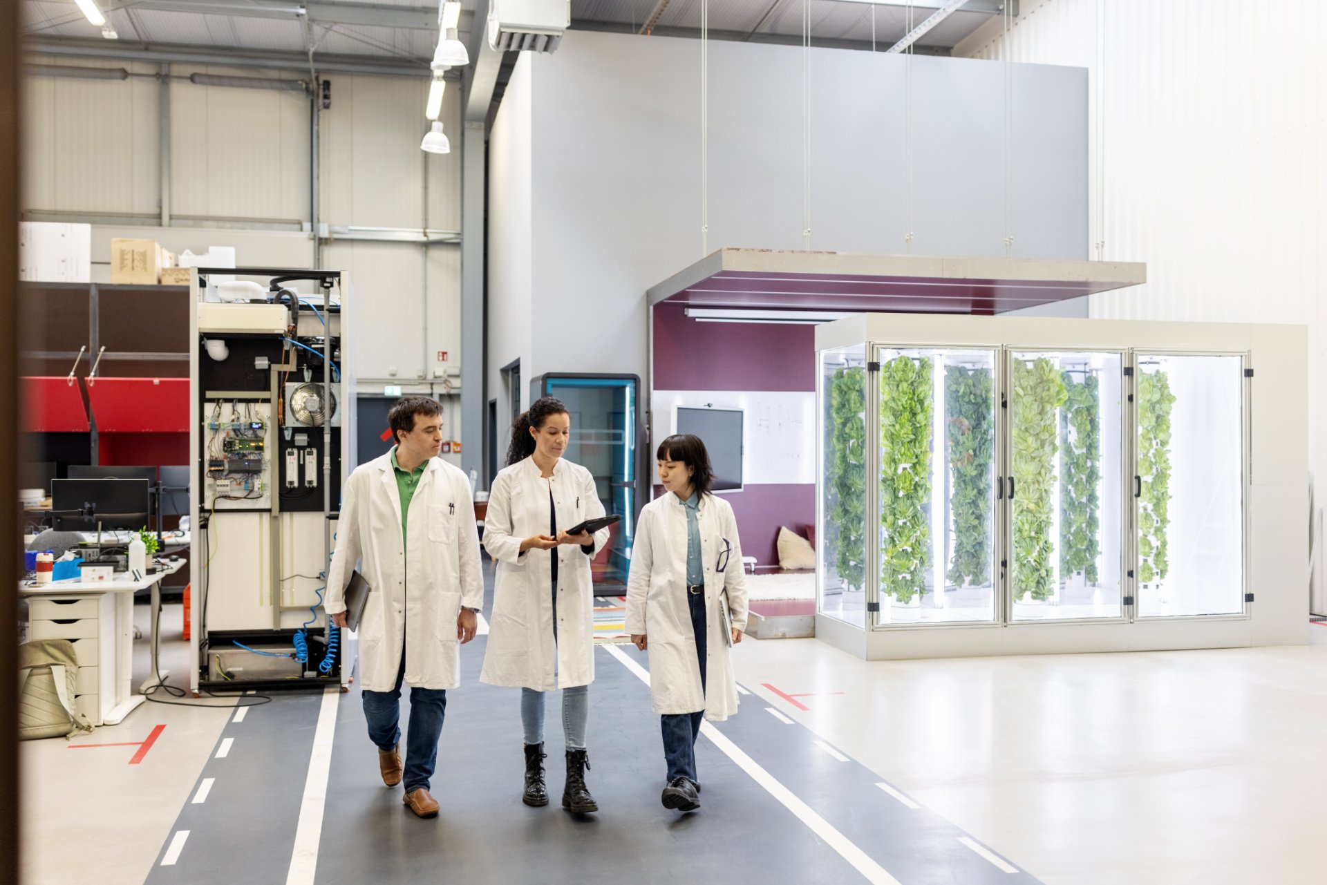 Three researchers in lab coats walking in a modern laboratory space with indoor plants.