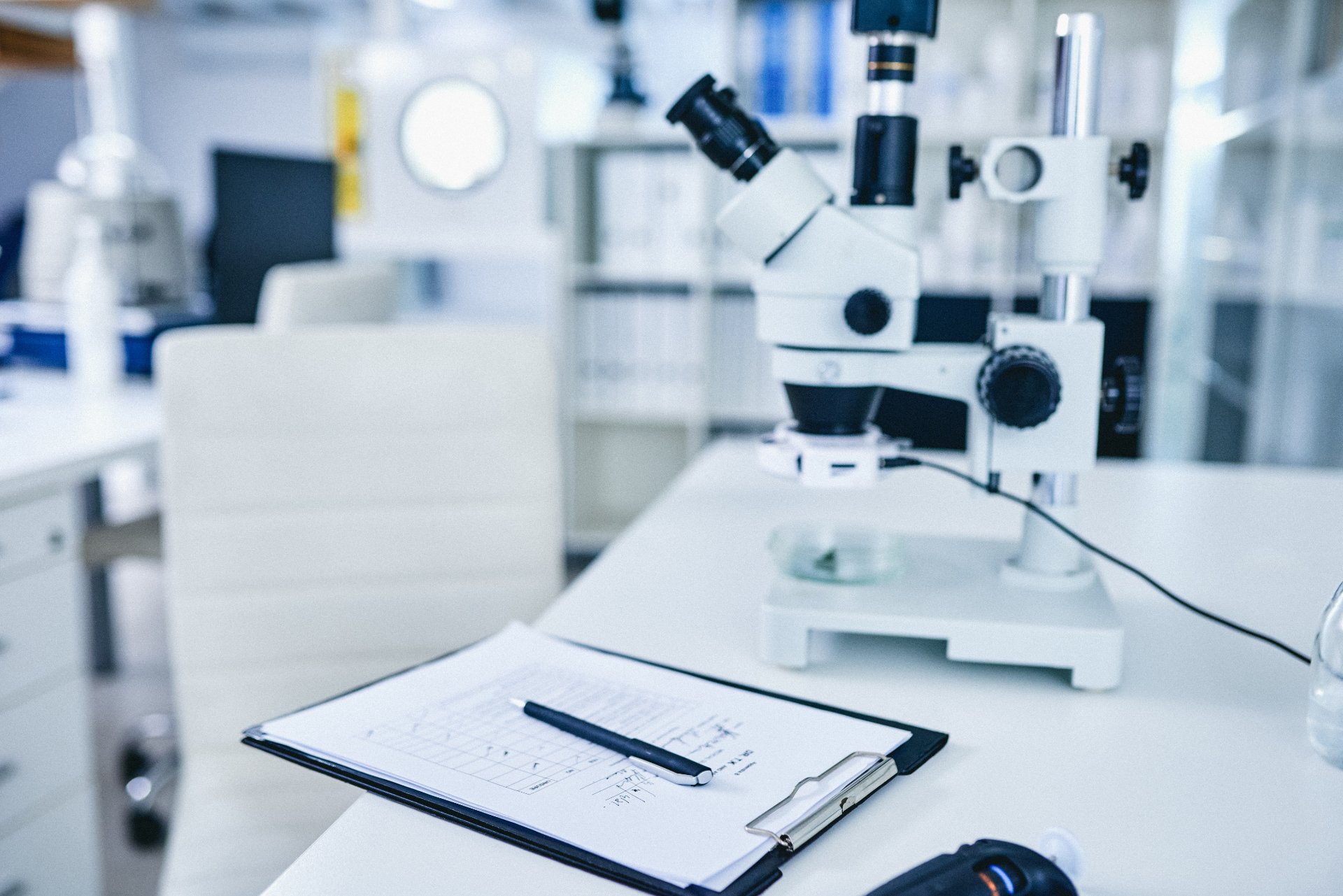 Microscope on a lab desk with a clipboard and pen in a modern research facility.